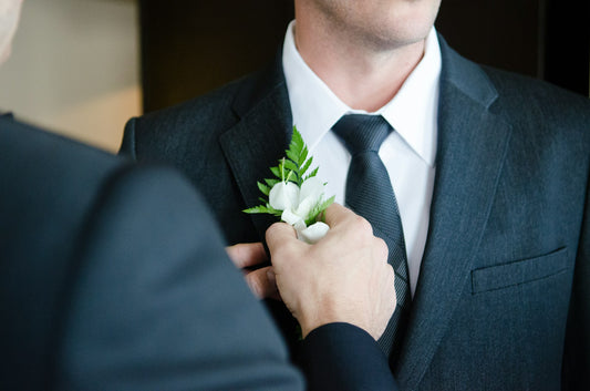Man putting boutonniere on groom's wedding tuxedo