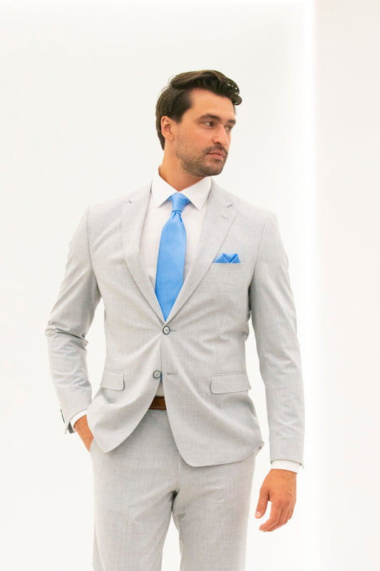Man wearing a silver gray suit with a blue tie and pocket square on a white background looking to the distance. 