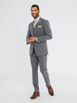 Man facing camera smiling wearing a three piece medium grey jacket, medium grey vest, medium grey pants, a sage tie, sage pocket square, sage lapel pin, and cognac shoes. Grooms Club. 